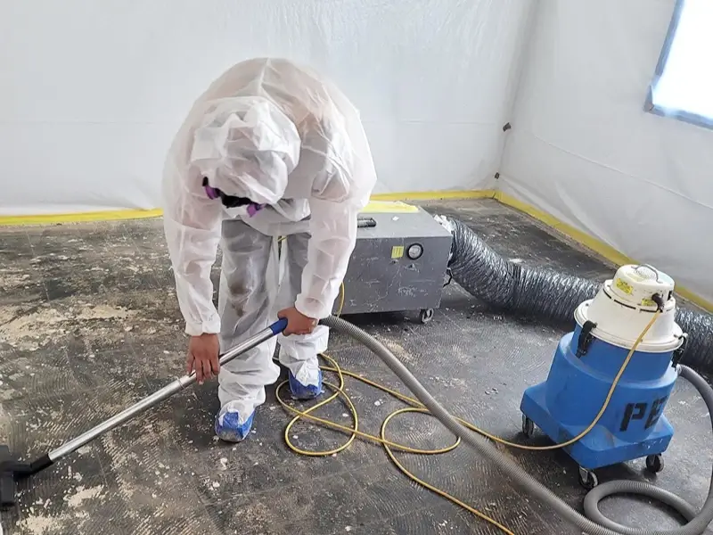 Worker in protective suit vacuuming a floor during cleanup.