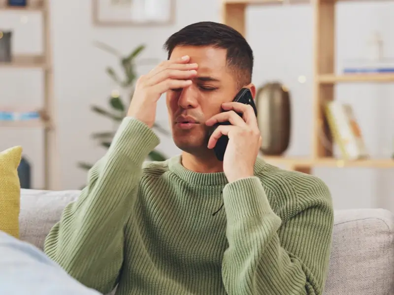 Man holding his forehead while talking on a phone, looking stressed.