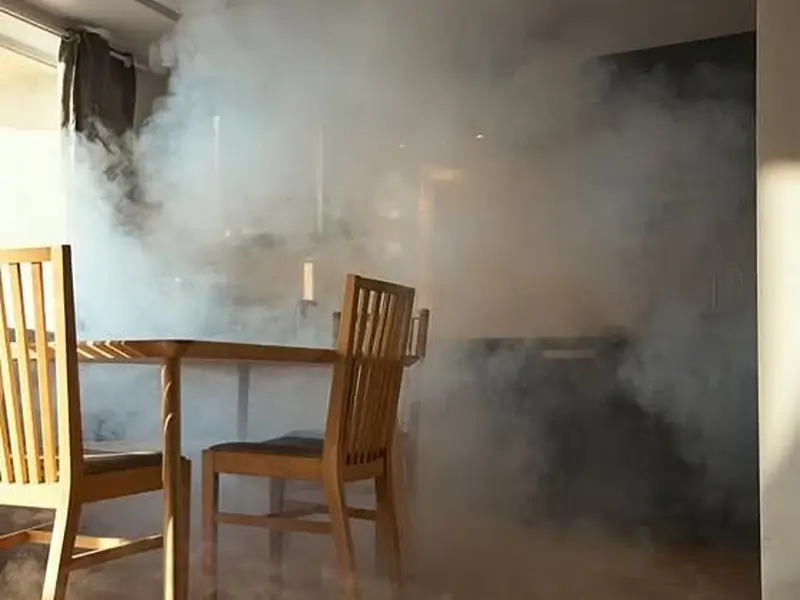 Smoke-filled dining room with wooden chairs and table.